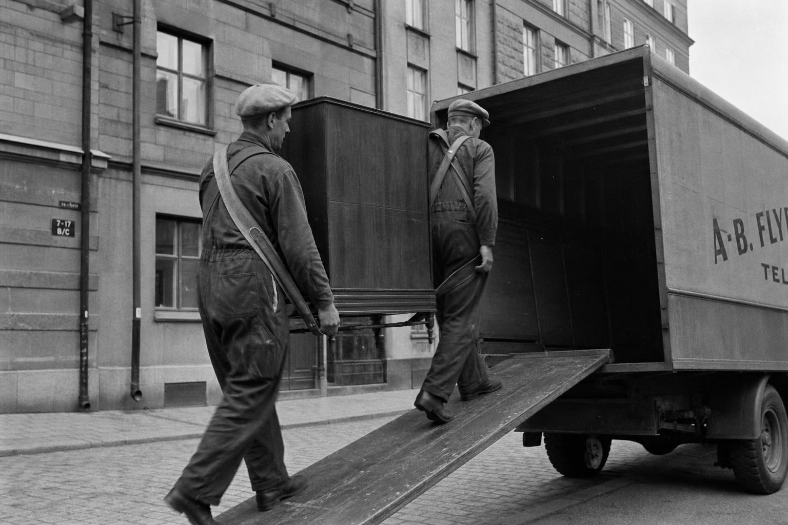 Flyttgubbar lastar en flyttbil från 1950-talet på en kullerstensgata i Skåne